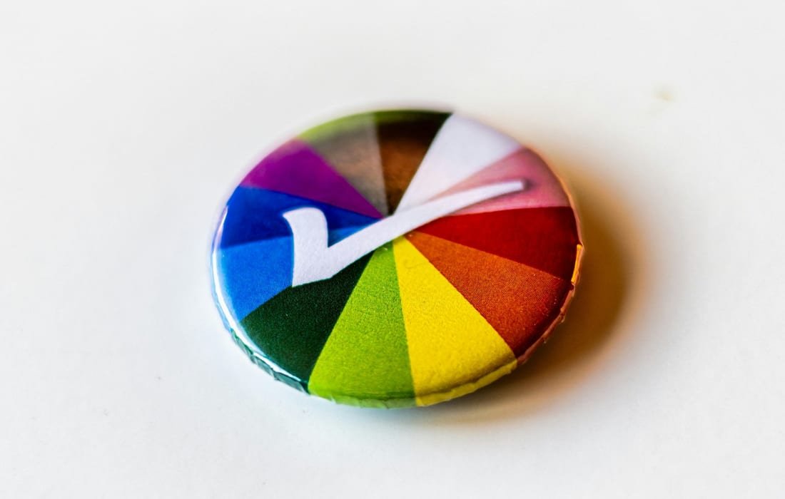 A round badge printed with a colour wheel and a white tick, lying on a white surface