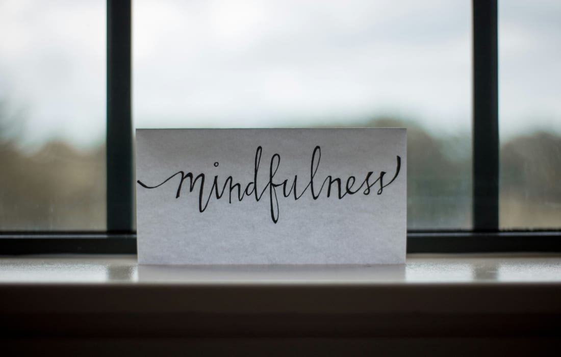 A handwritten card reading mindfulness, standing on a windowsill against a soft grey sky
