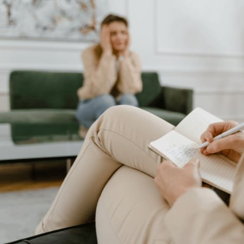 A person on a sofa writing in a notebook beside a cup of tea