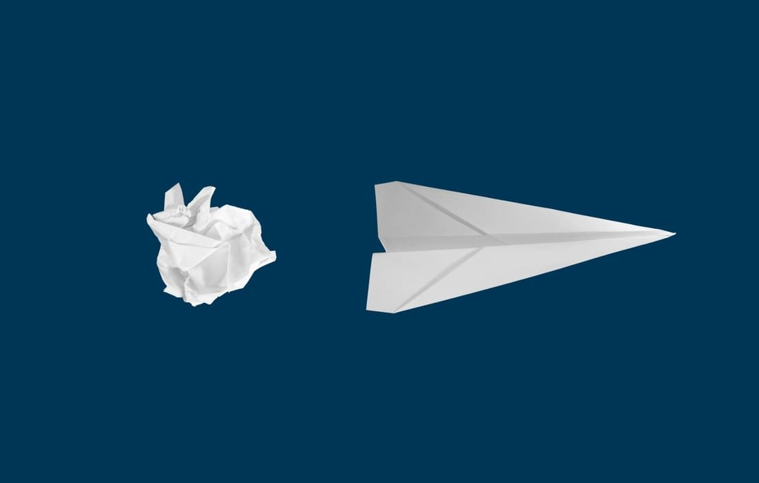 A crumpled ball of paper beside a folded paper plane, on a deep blue ground